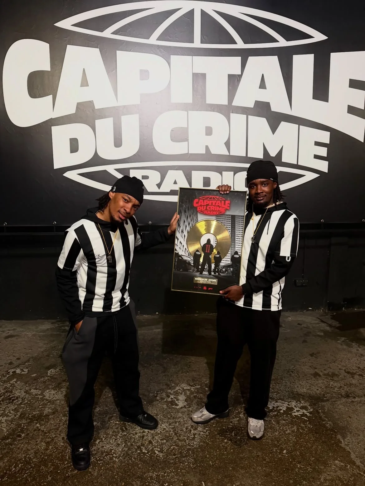 Jey et D2 tenant le disque d'or Capitale du Crime Radio, devant le logo de la radio