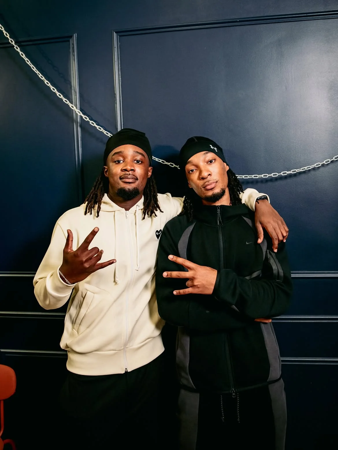 Jey et D2, en survêtement, devant un mur bleu nuit